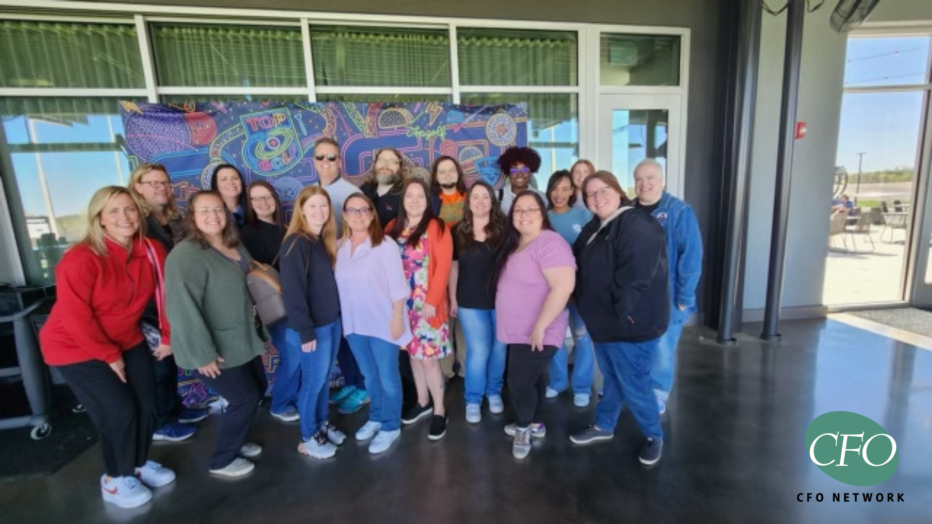 CFO Cares team are posing for a picture in front of a mosaic wall.