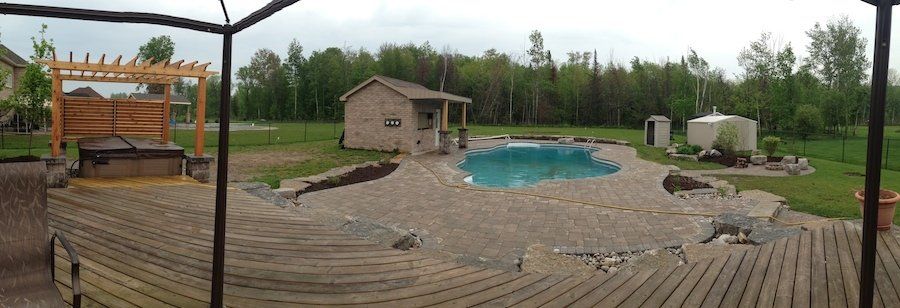 A large swimming pool is surrounded by a wooden deck and a gazebo.