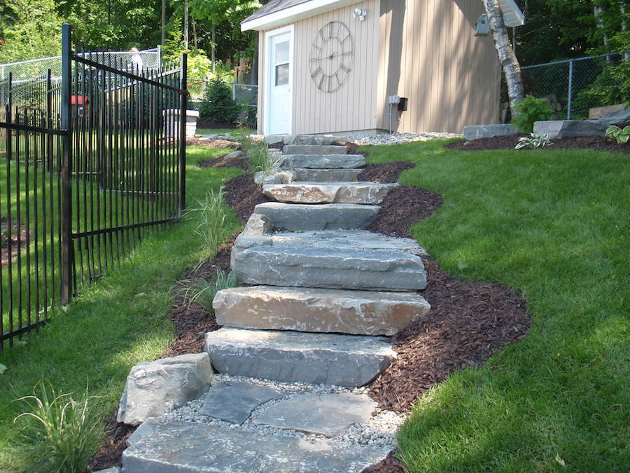 A stone walkway leading to a shed with a clock on the wall