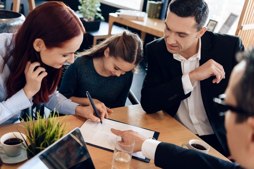 A Family is Sitting at a Table Signing a Document — McVittie Legal In Ballina, NSW