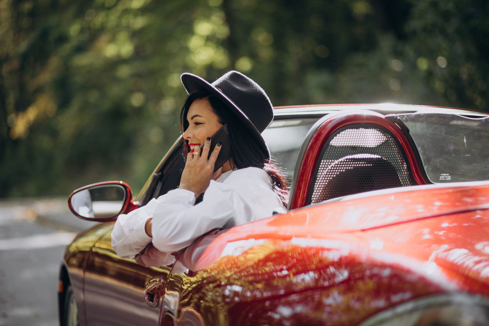 A woman is sitting in a red car talking on a cell phone.