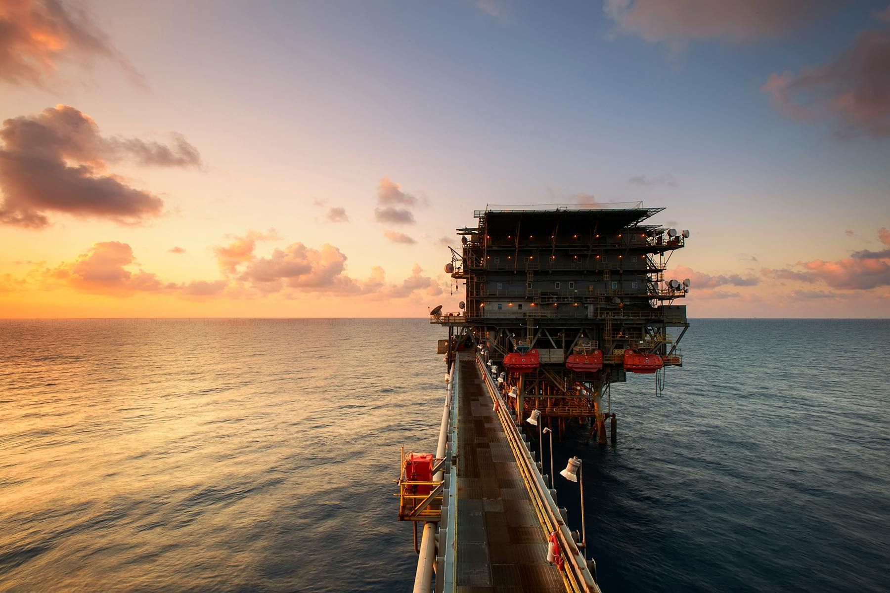 An oil rig in the middle of the ocean at sunset.