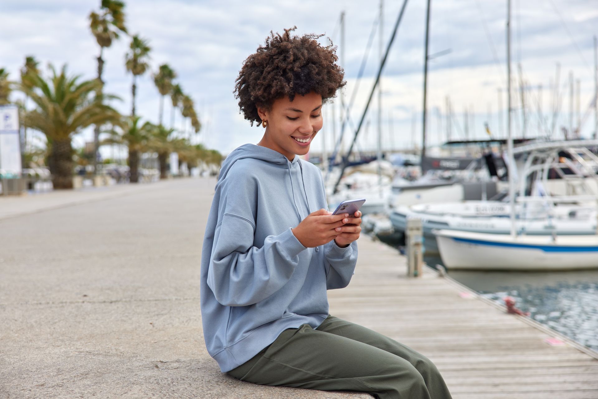 A woman is sitting on a pier looking at her cell phone.