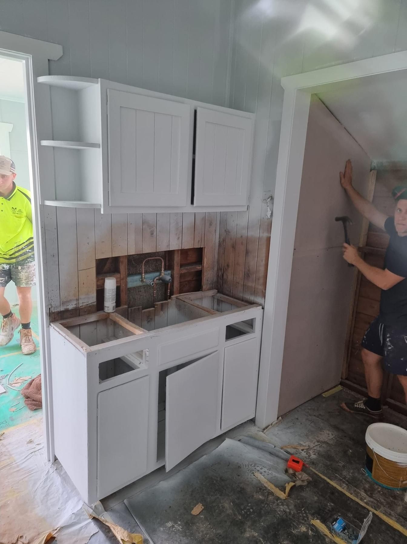 A Man Is Working On A Kitchen With White Cabinets And A Sink — LMS Painting & Maintenance Pty Ltd In Maitland, NSW
