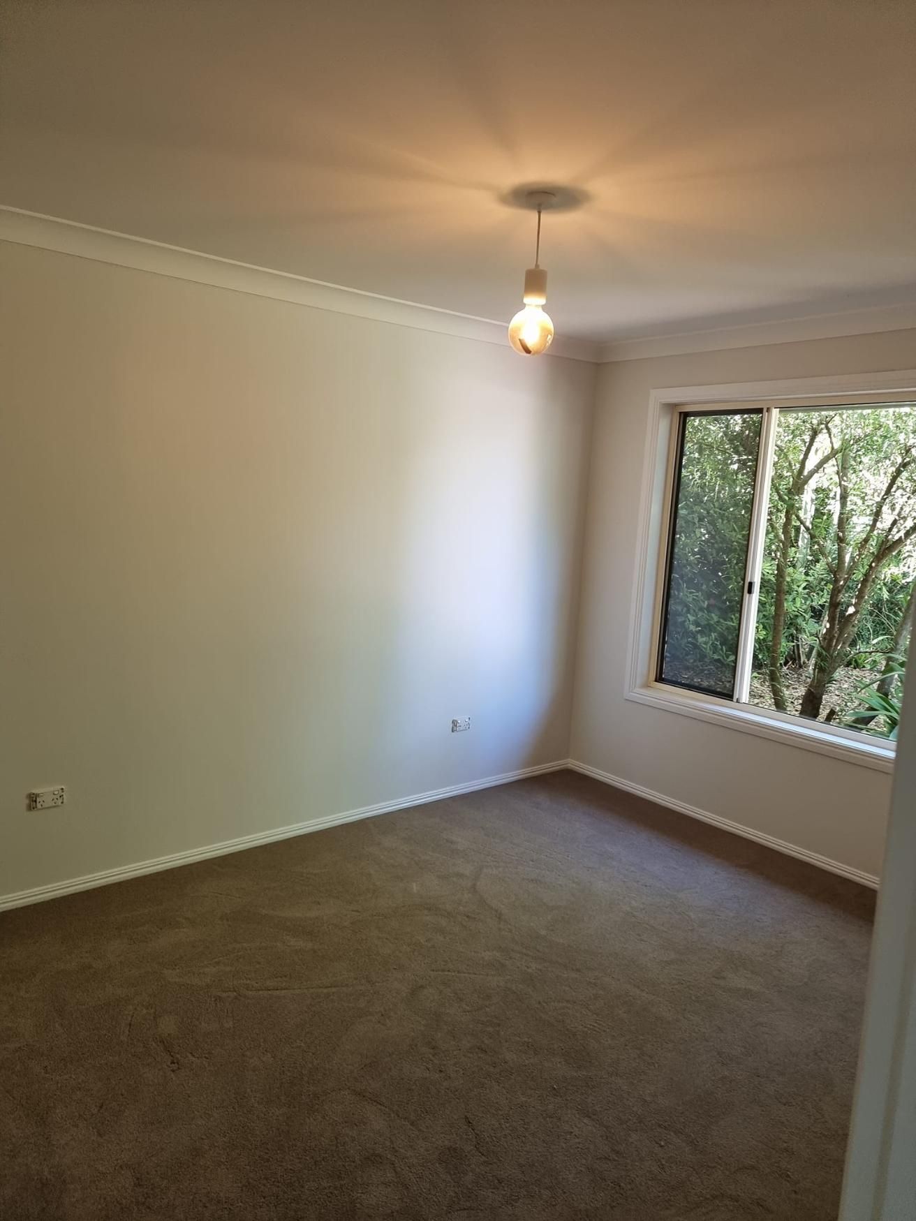 An Empty Room With A Window And A Light Hanging From The Ceiling — LMS Painting & Maintenance Pty Ltd In Maitland, NSW