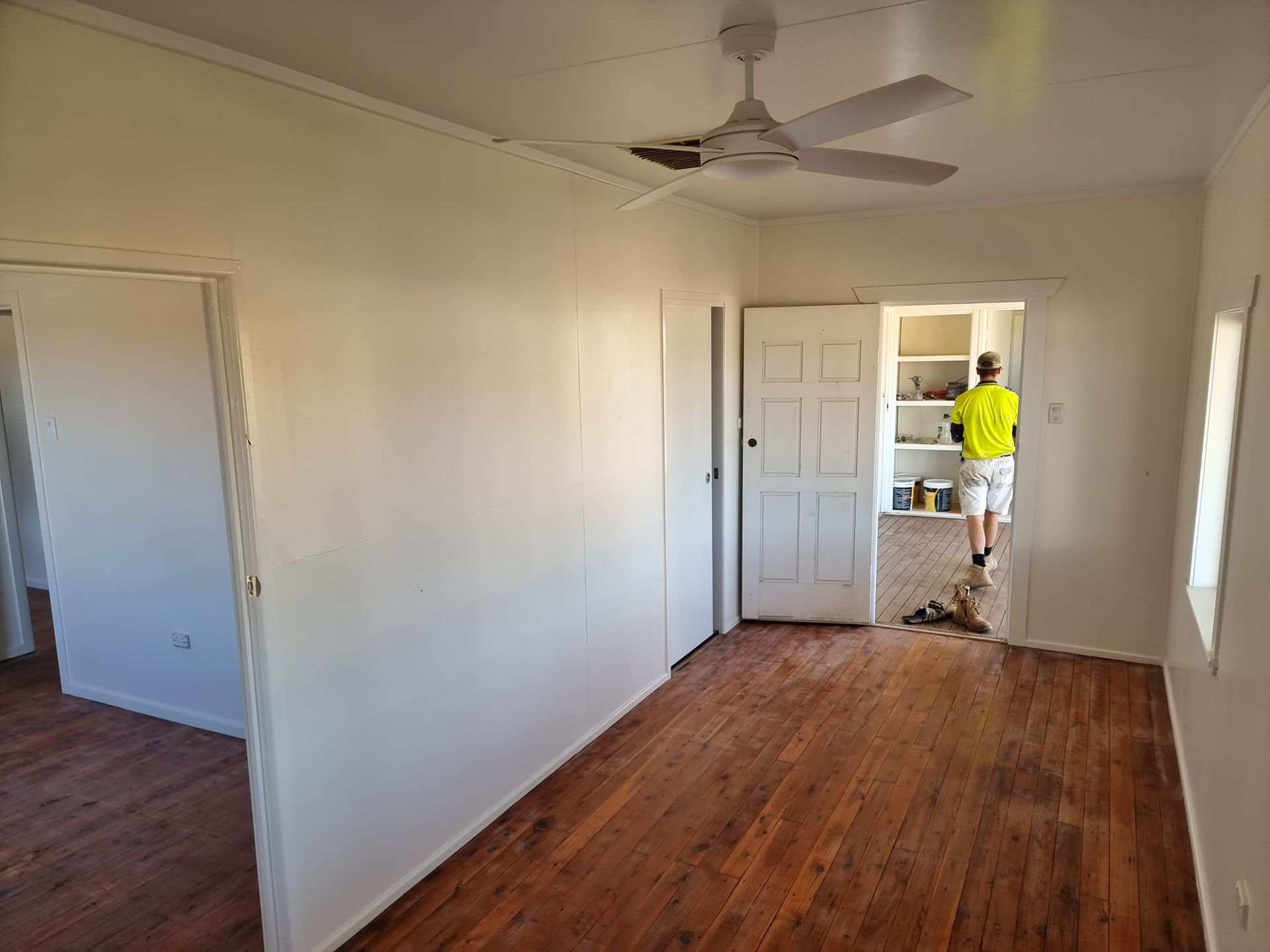 A Man Is Standing In An Empty Room With A Ceiling Fan — LMS Painting & Maintenance Pty Ltd In North Lambton, NSW