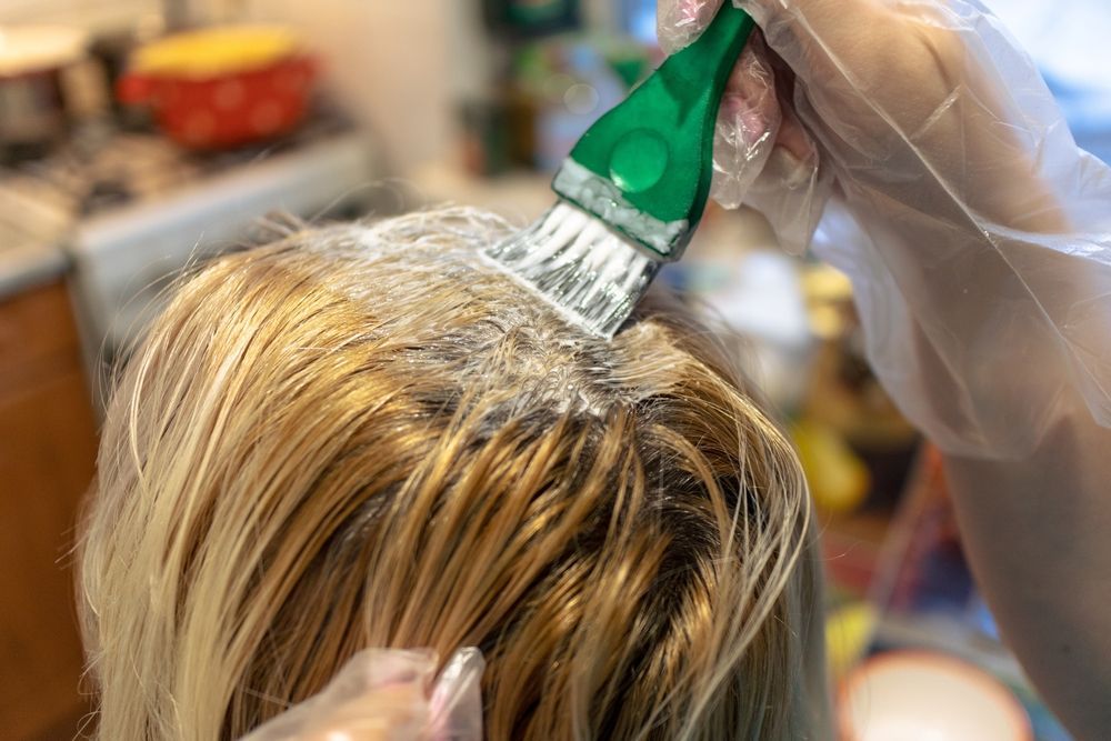 A woman is getting her hair dyed with a green brush.