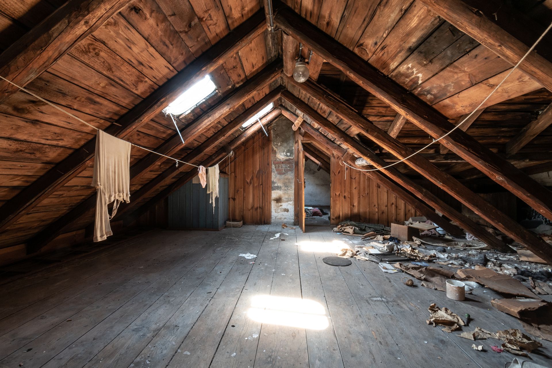 Old attic with wood beams, worn floor, sunlight through openings, and debris.
