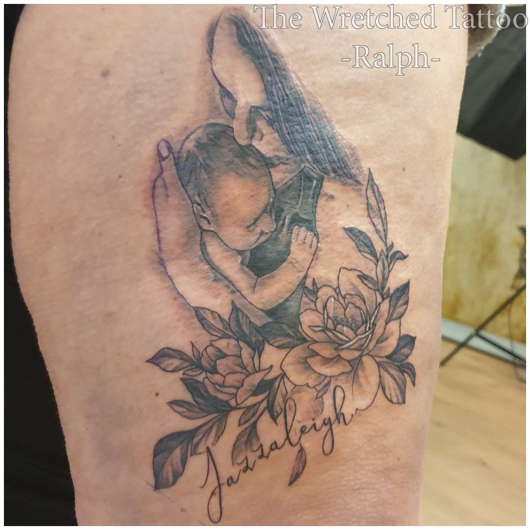Een vrouw heeft een tatoeage van een baby en bloemen op haar been.