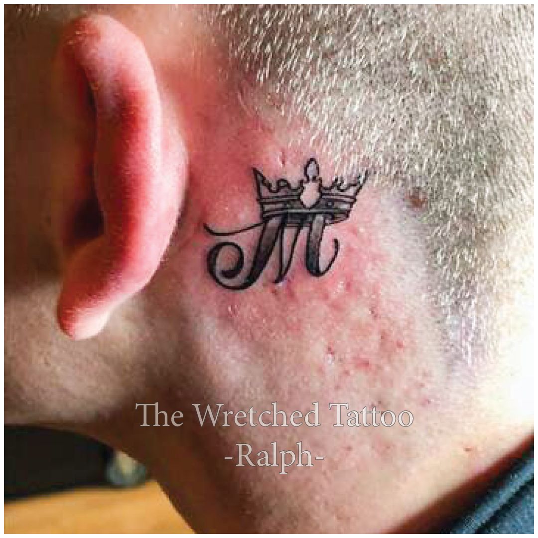 Een man heeft een tatoeage van een kroon en de letter m achter zijn oor.