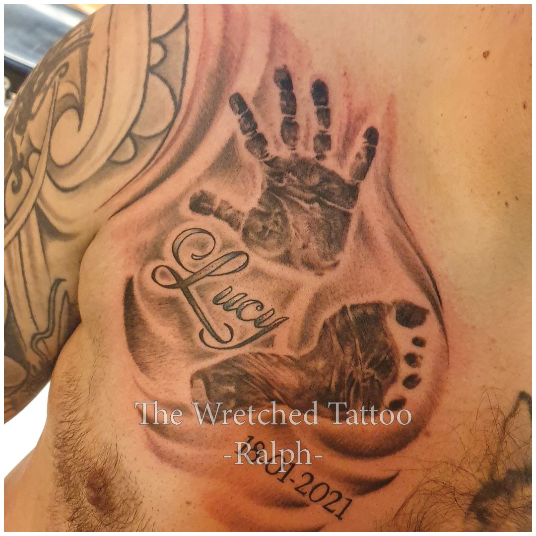 Een man heeft een tatoeage op zijn borst van een baby handje en voet met de nam Lucy