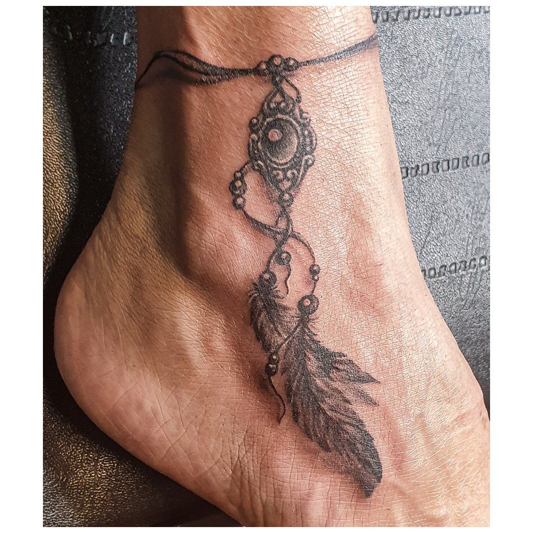 Een persoon heeft een tatoeage van een dromenvanger en veren op zijn enkel.
