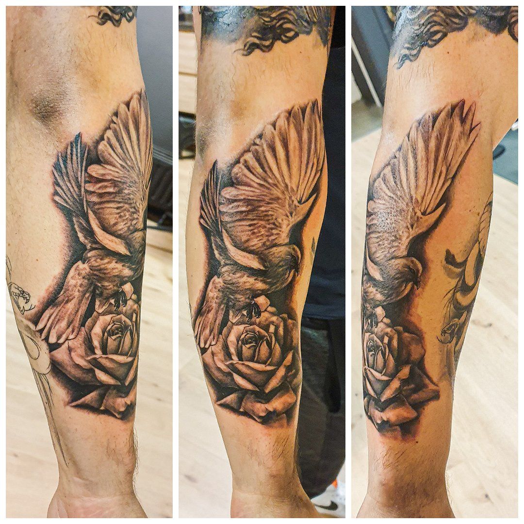 Een man heeft een tatoeage van een duif en rozen op zijn arm