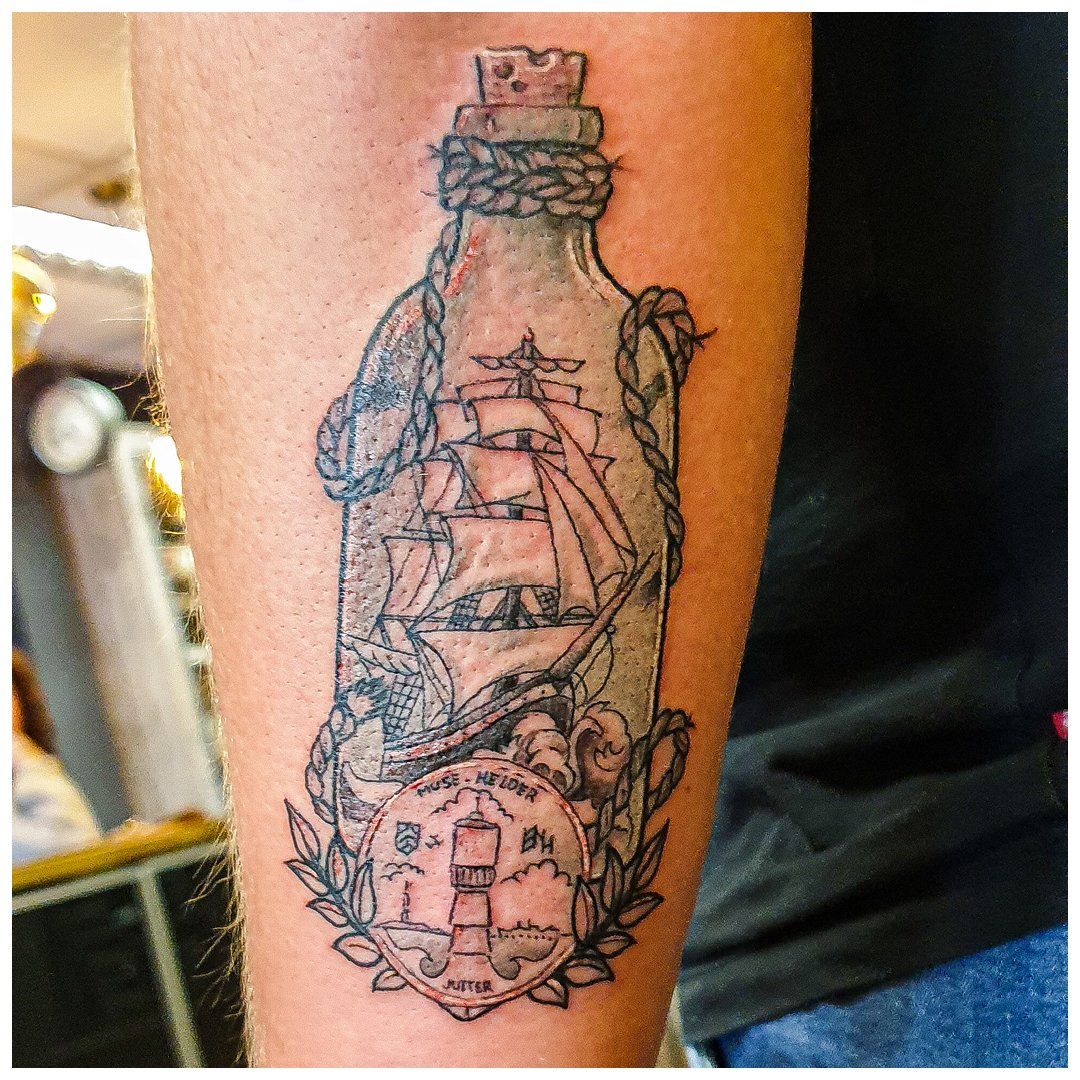 Een tatoeage van een schip in een fles op iemands arm