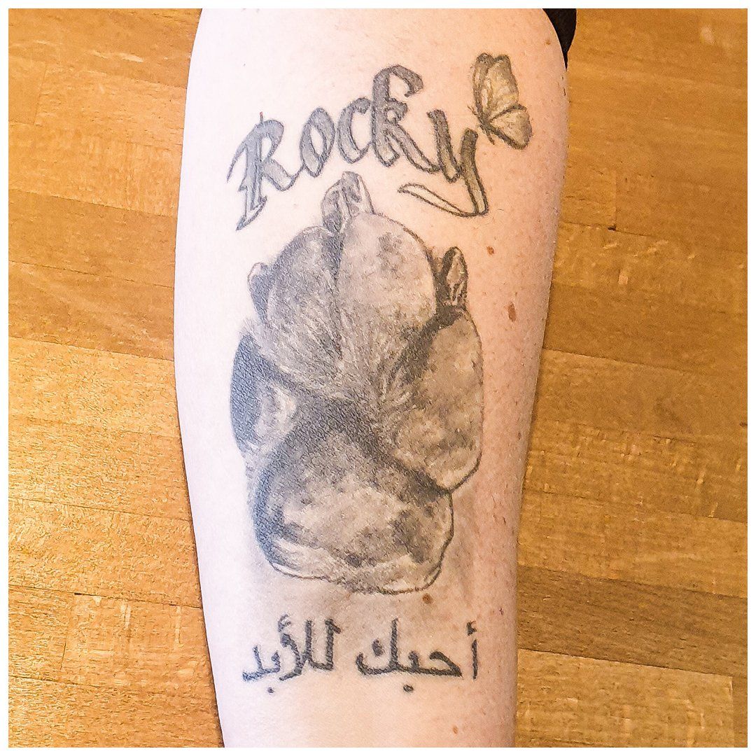 Een persoon heeft een tatoeage op zijn been met de tekst rocky