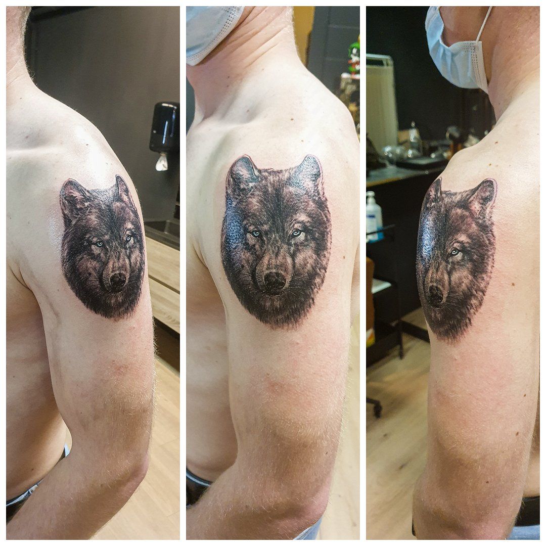 Een man heeft een tatoeage van de kop van een wolf op zijn schouder.