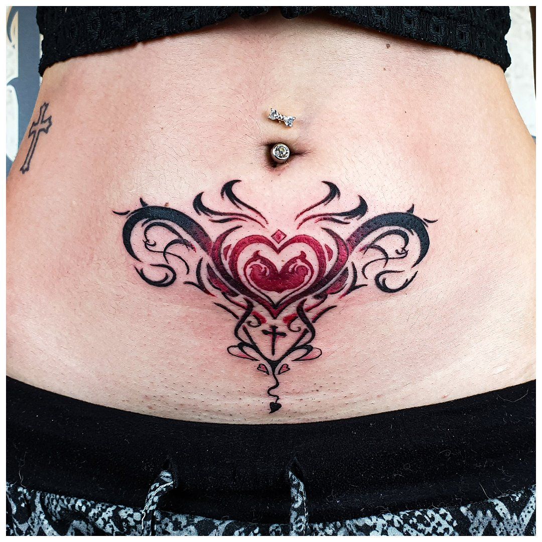 Een vrouw heeft een tatoeage op haar buik met een hart en een kruis.