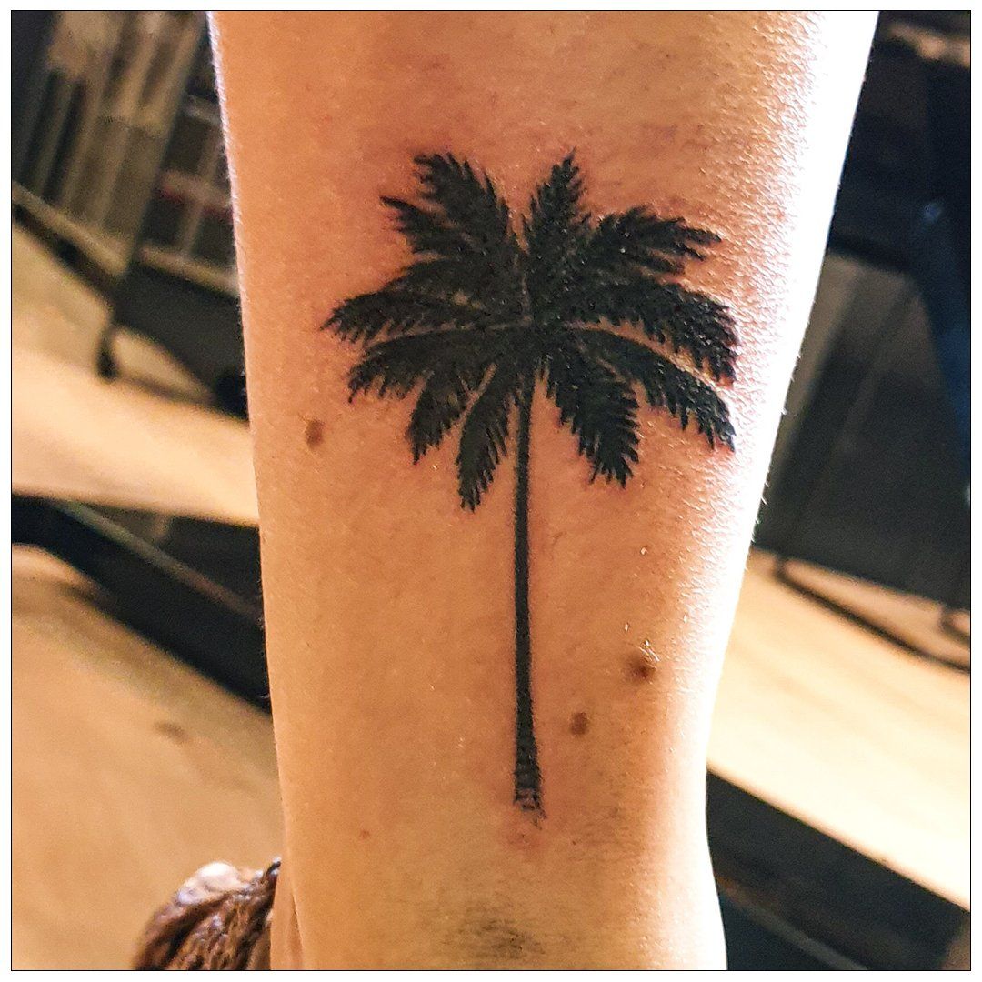 Een persoon heeft een tatoeage van een palmboom op zijn been