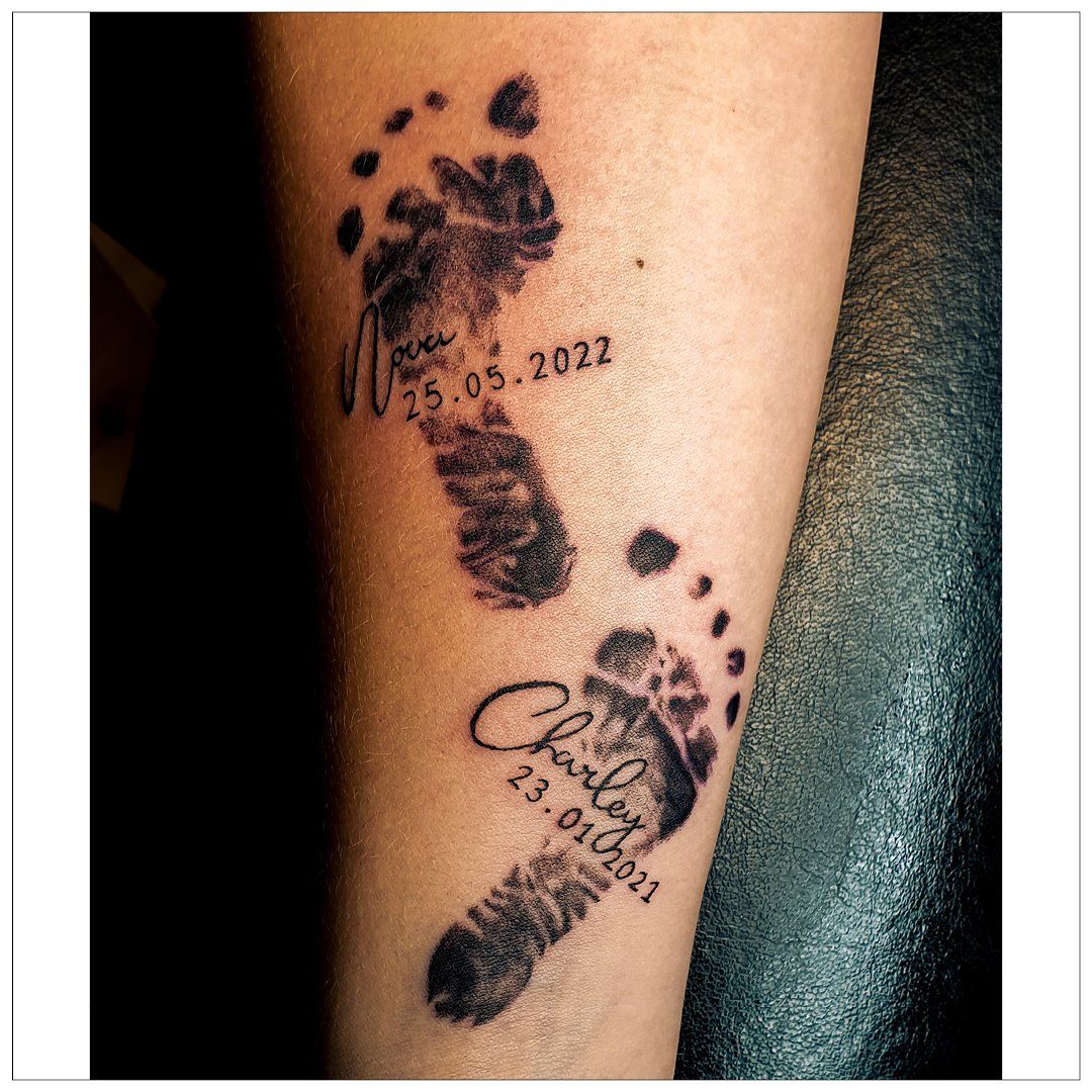 Iemand heeft een tatoeage van de voetafdrukken van zijn baby op zijn been.