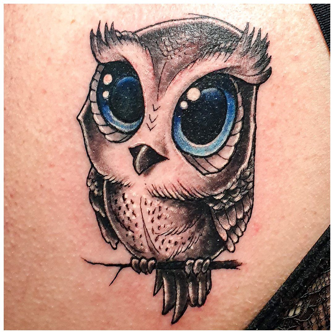 Een tatoeage van een uil met grote blauwe ogen zittend op een tak.