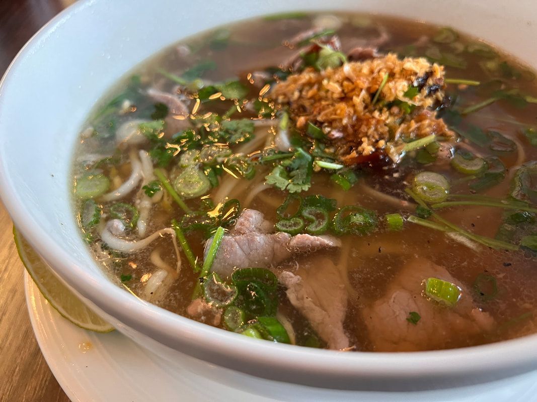 Restaurant exterior with two men seated, motorbike parked.  Pink awning, white building.