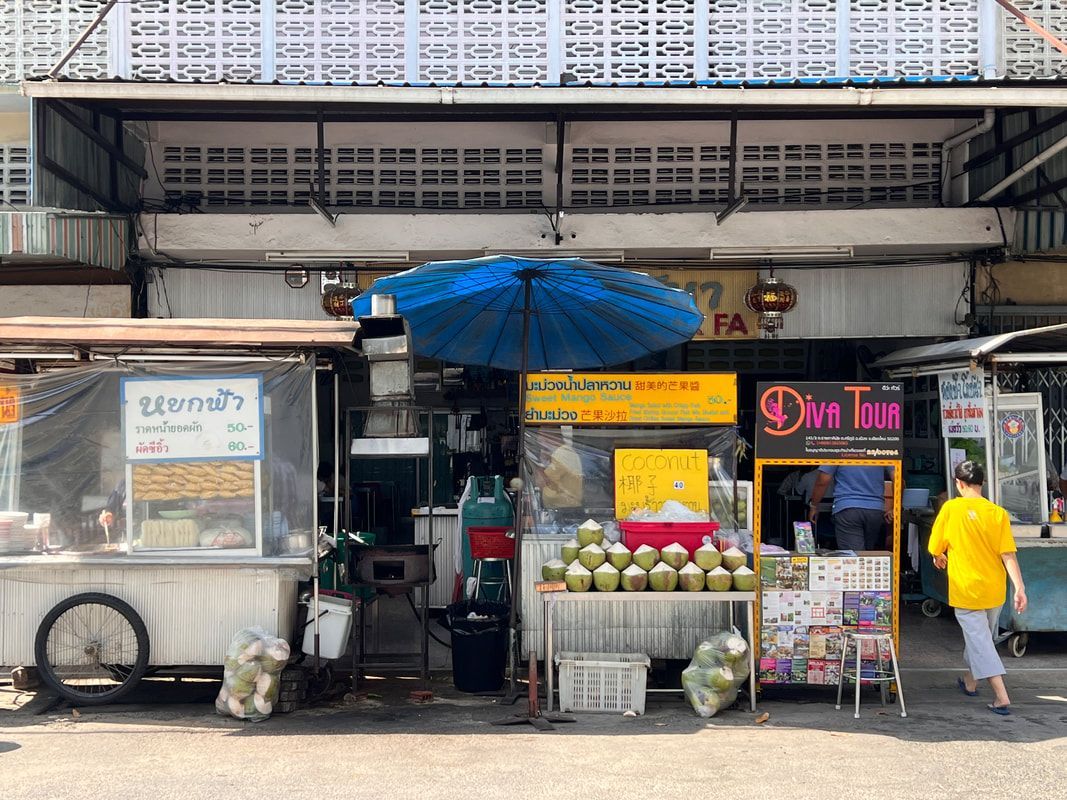 Street vendors selling food and drinks in front of a weathered building; a person in yellow walks by.