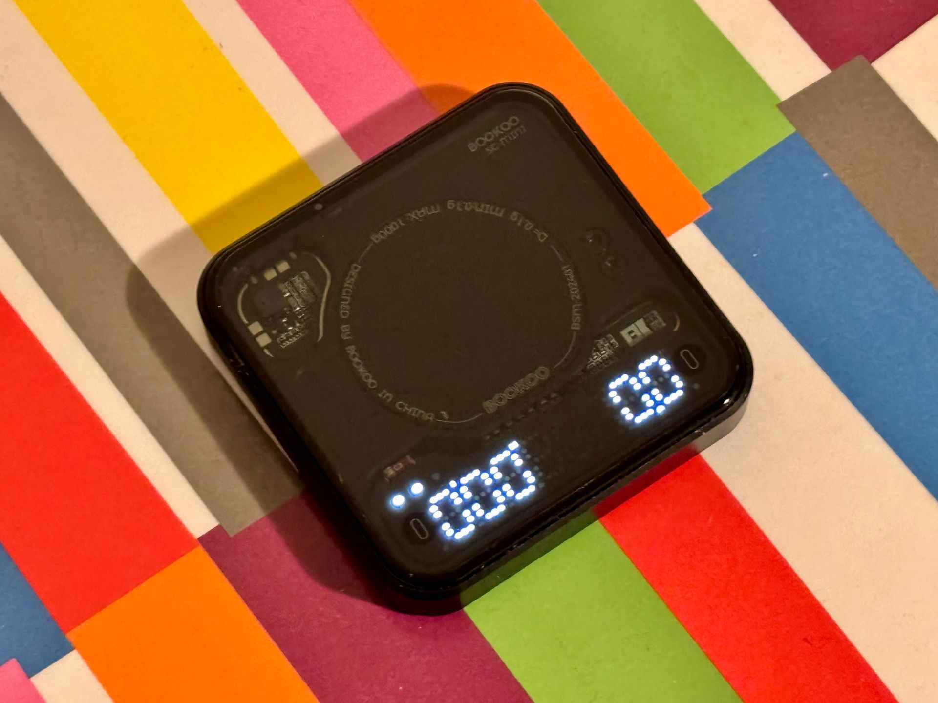 Black digital kitchen scale on a textured, light-brown surface, displaying weight and timer.