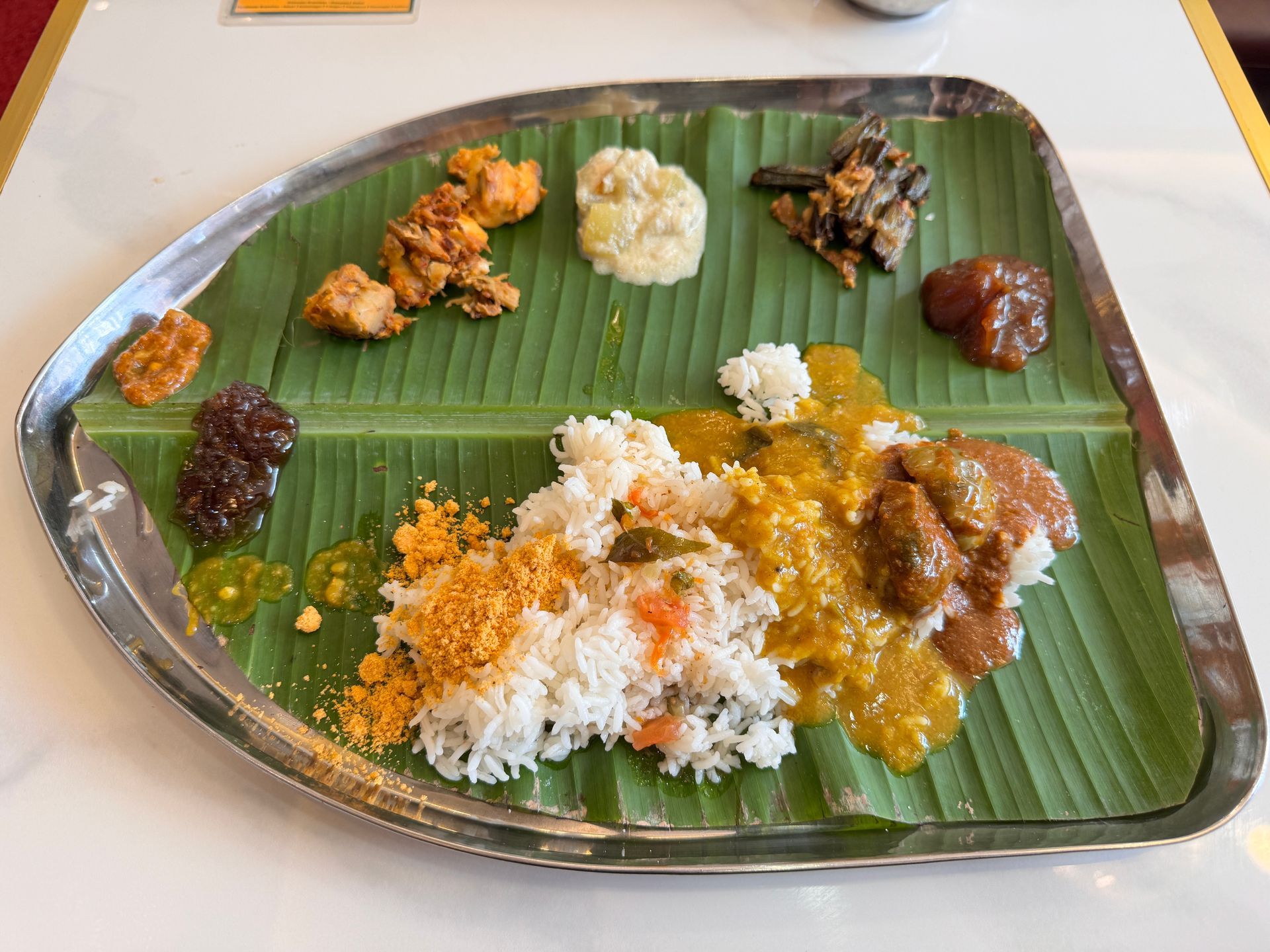 South Indian thali meal on a banana leaf-lined tray. Rice, curry, and various side dishes are arranged.