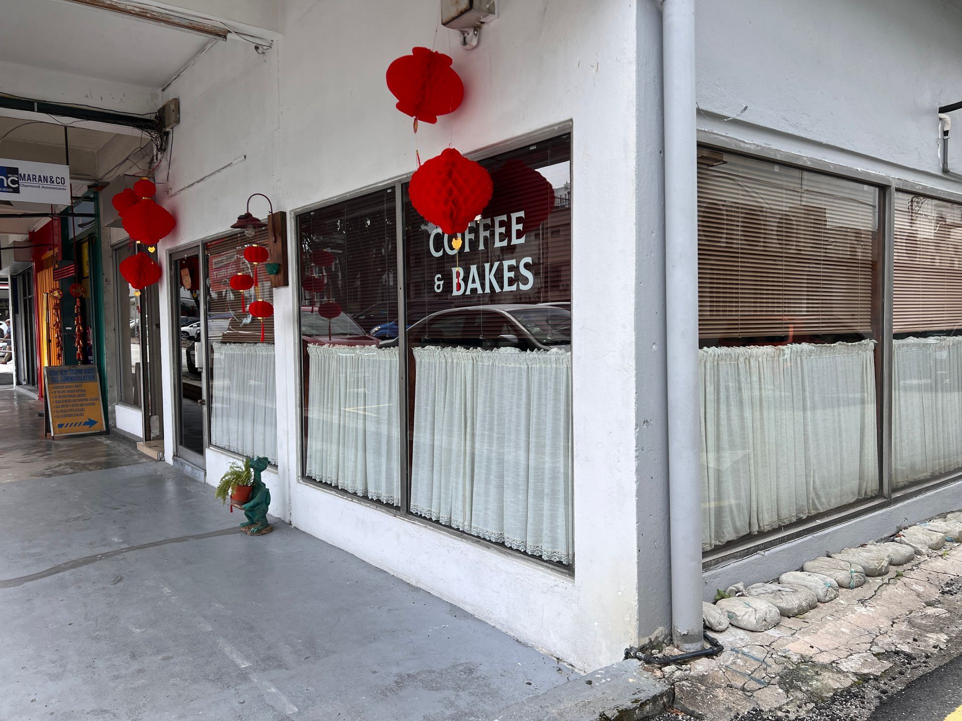 Coffee & Bakes shop corner exterior, decorated with red lanterns. White building with windows, street view.