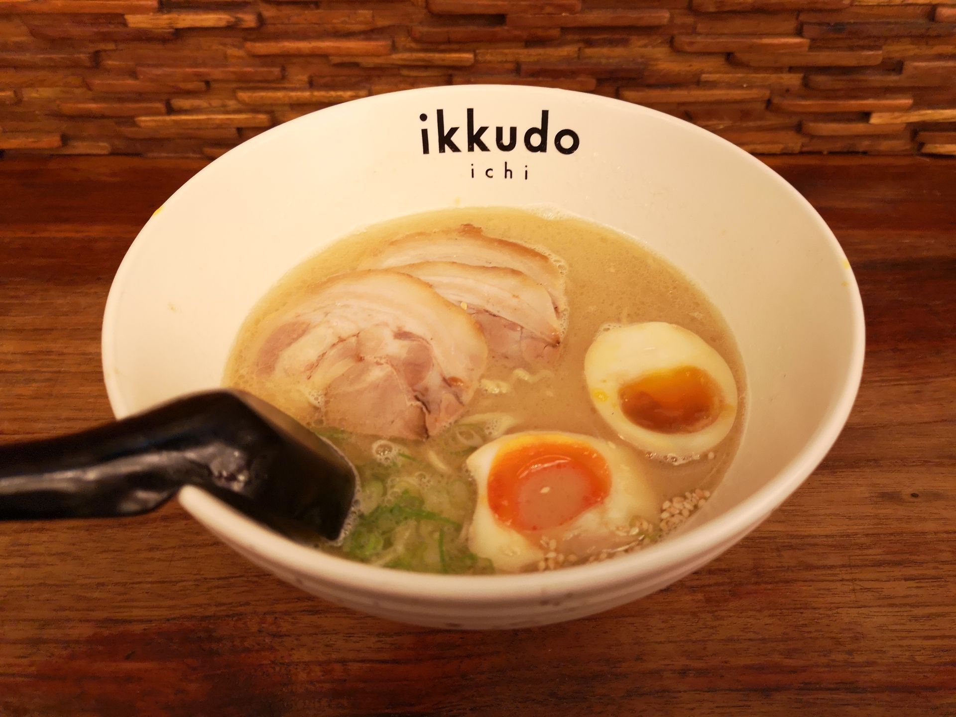 Ramen bowl with pork slices and soft-boiled eggs.  Black spoon rests on the edge.
