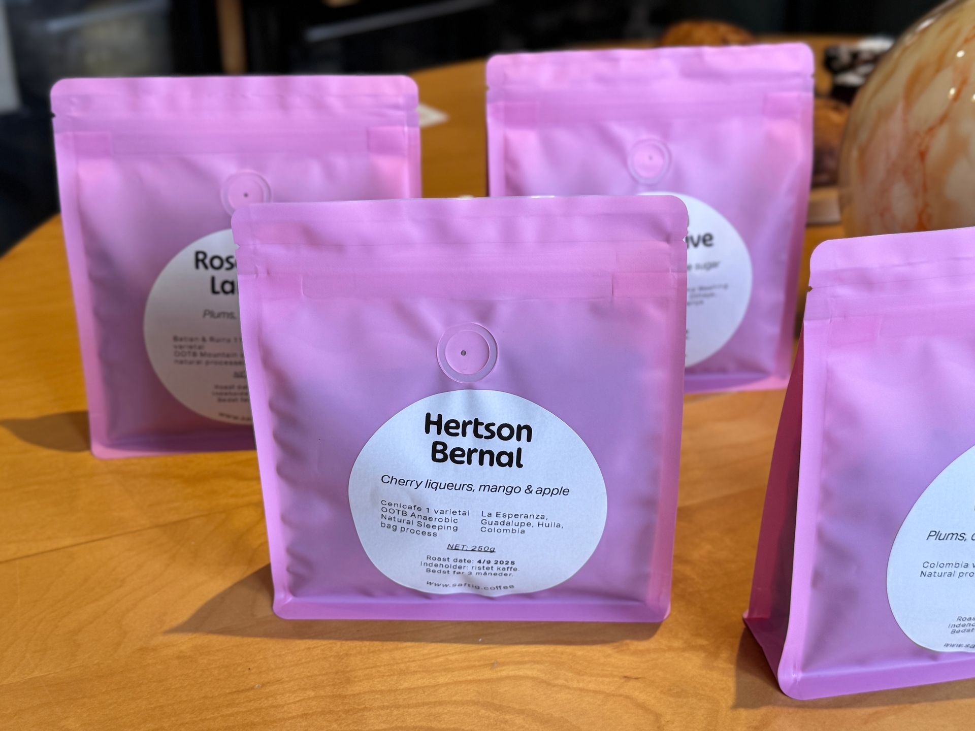 Three bags of coffee with red polka dots in a wooden tray, alongside a chocolate card.