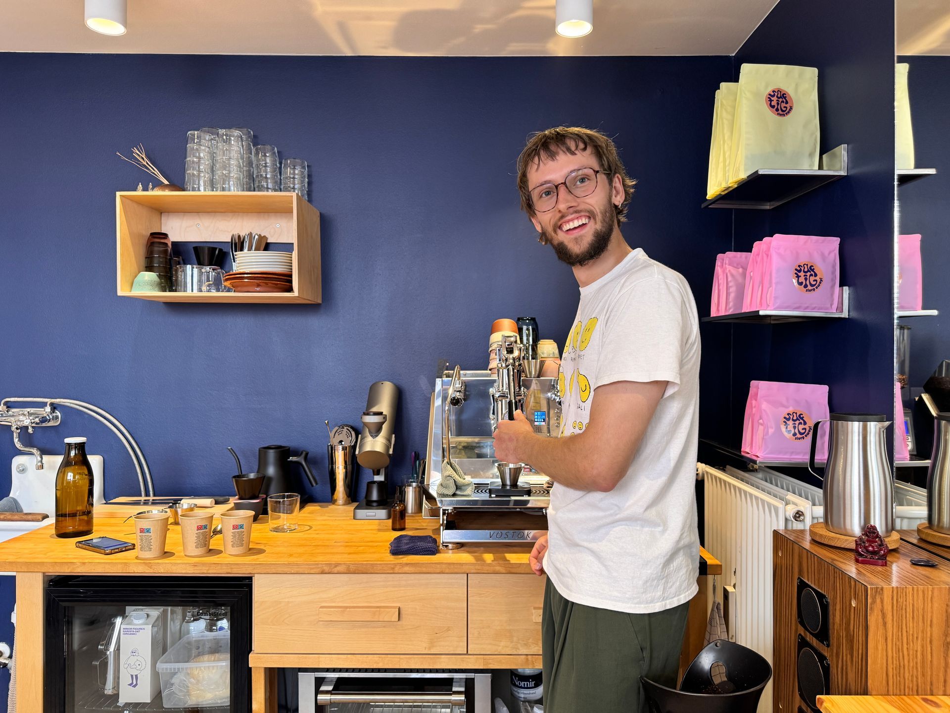 Restaurant exterior with two men seated, motorbike parked.  Pink awning, white building.