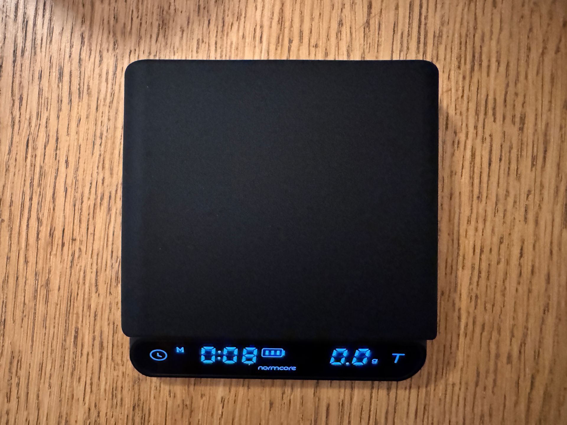 Black digital scale with blue display showing weight and timer on a wooden surface.