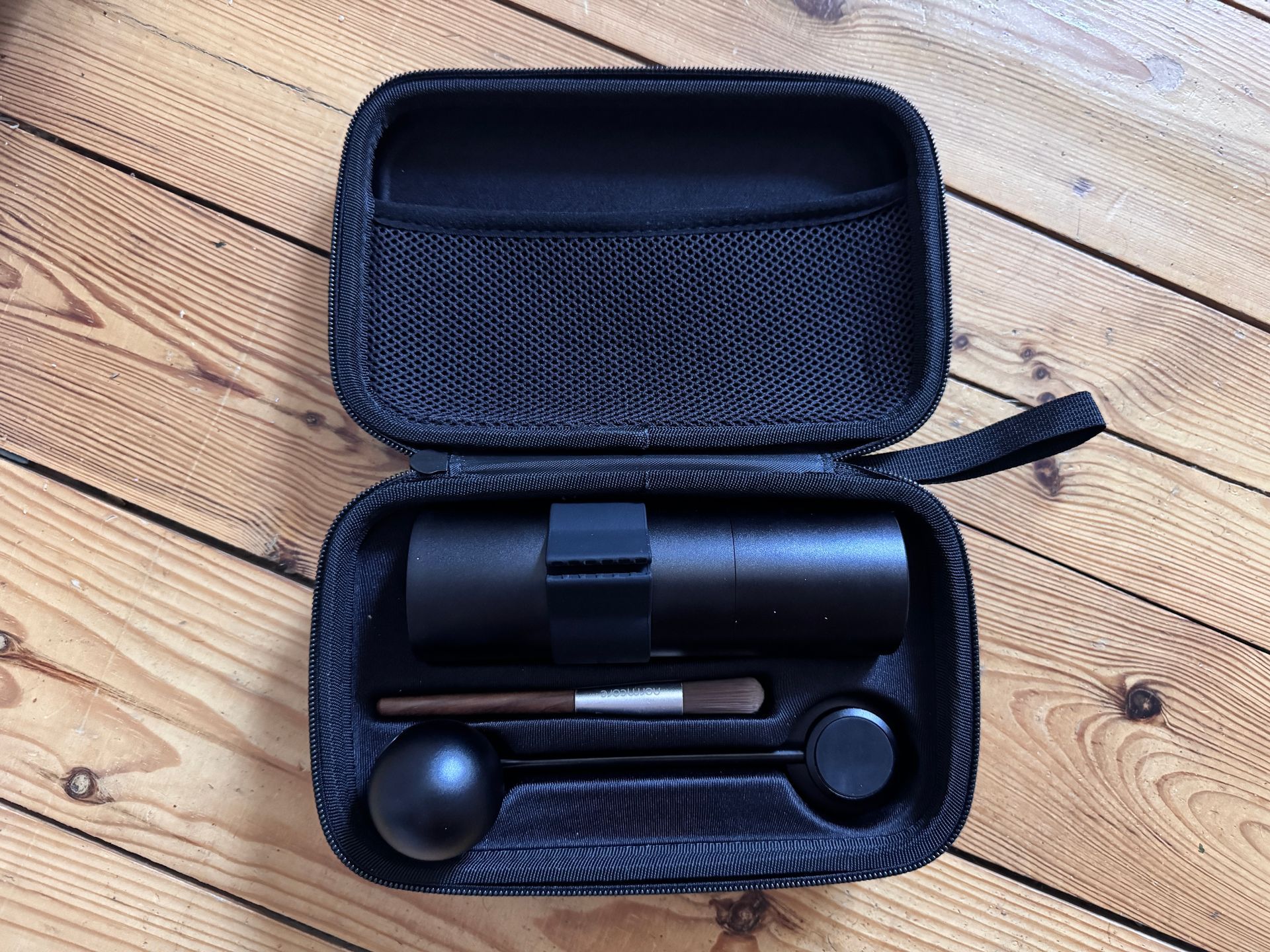 Black espresso maker and accessories in an open travel case on a wooden surface.