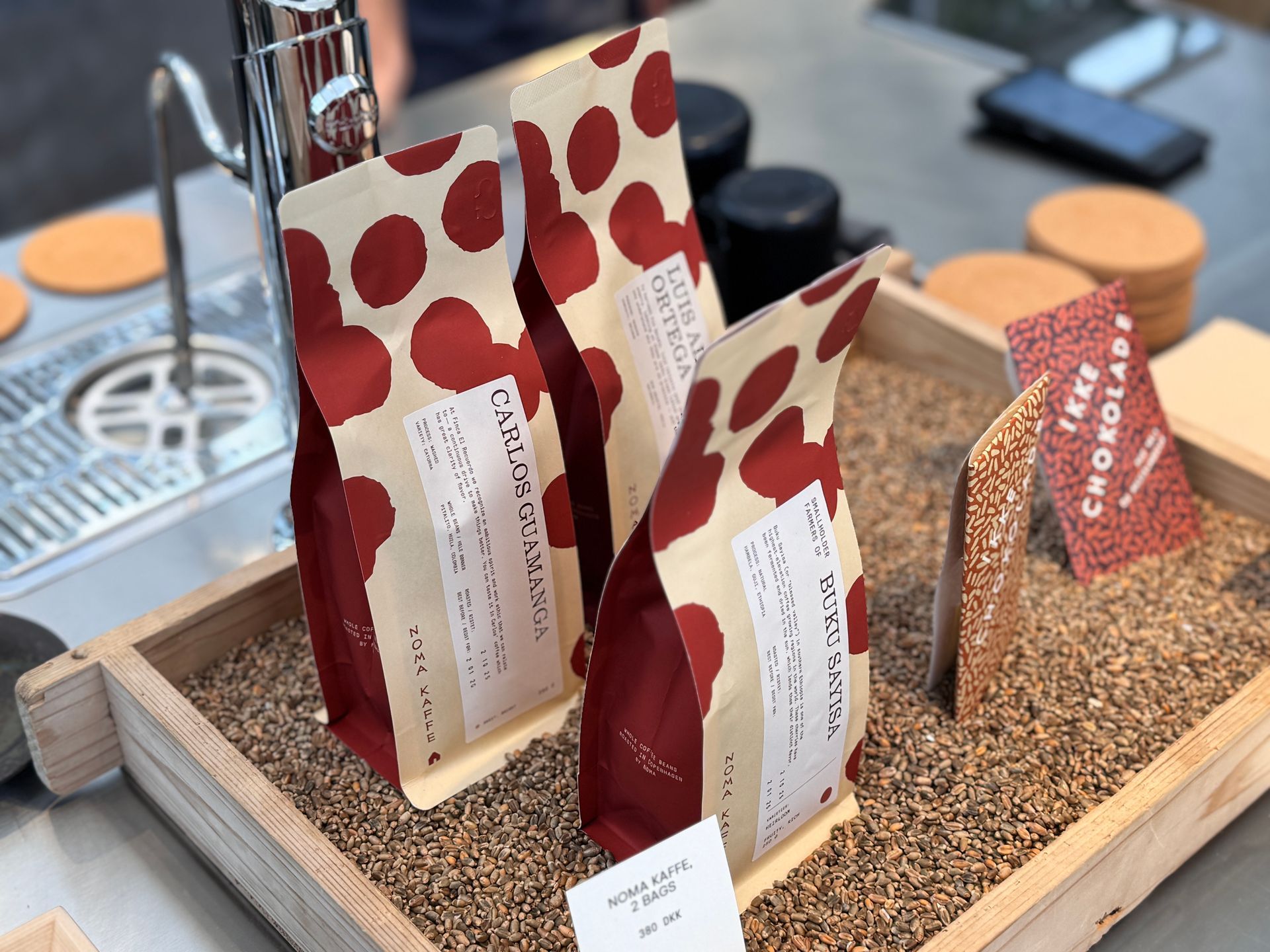 Three bags of coffee with red polka dots in a wooden tray, alongside a chocolate card.