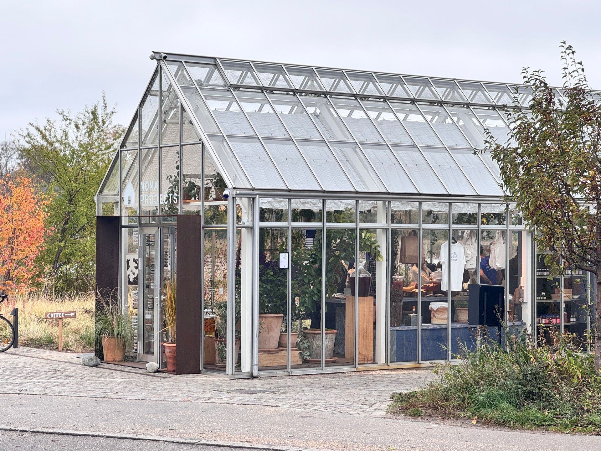 Glass greenhouse storefront, displaying plants and merchandise, on a gray day.