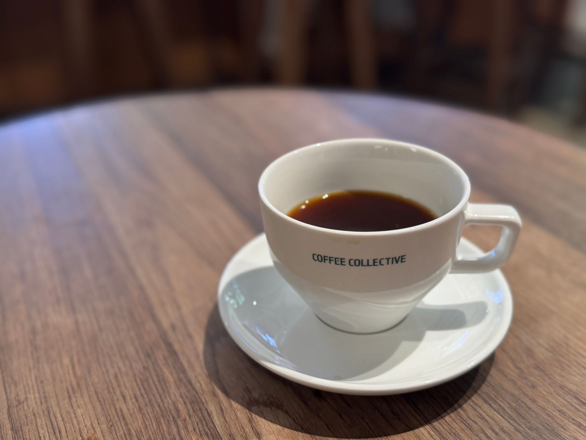 Coffee in a white mug on a saucer, on a wooden table. The mug says
