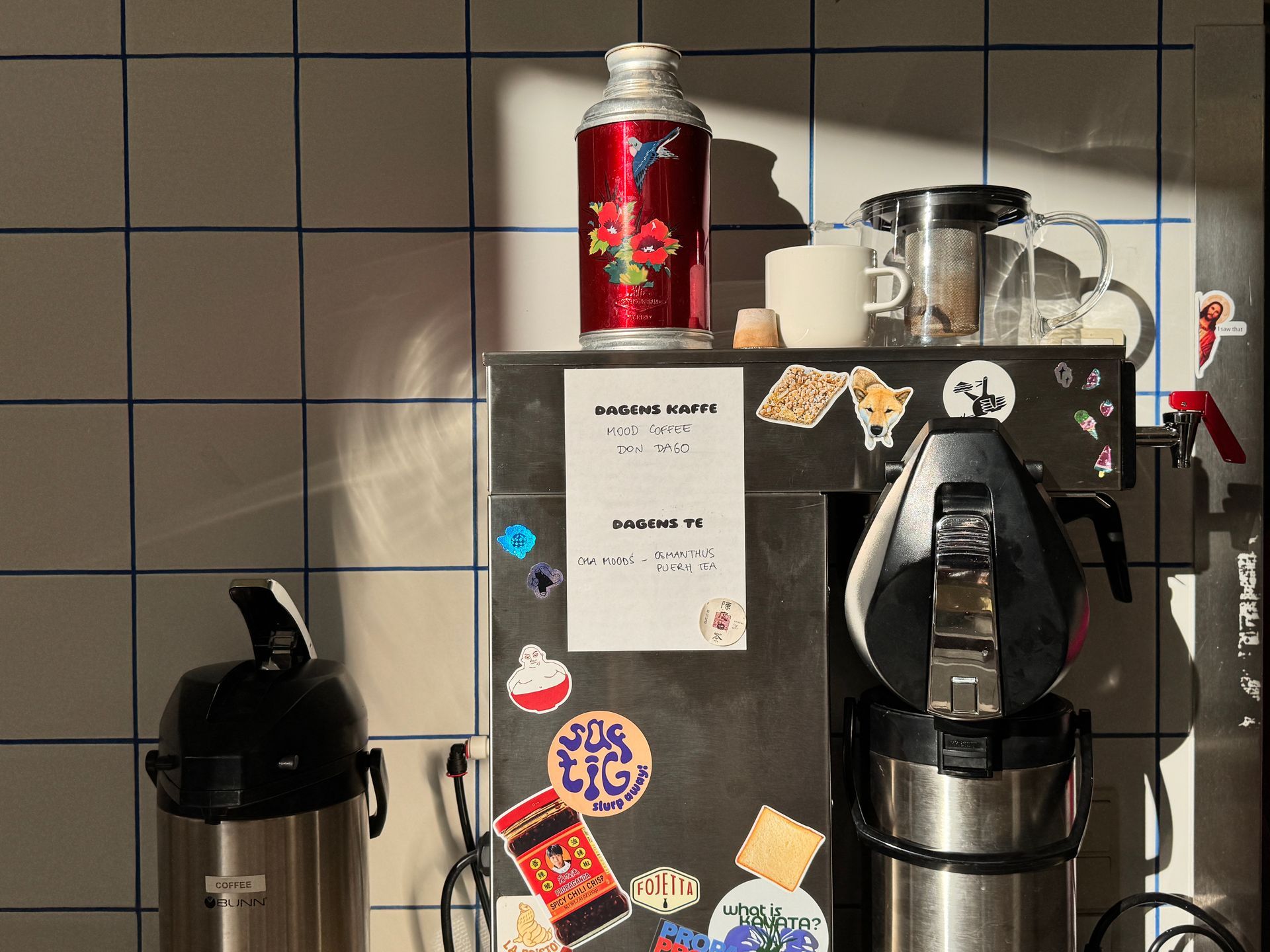 Restaurant exterior with two men seated, motorbike parked. Pink awning, white building.