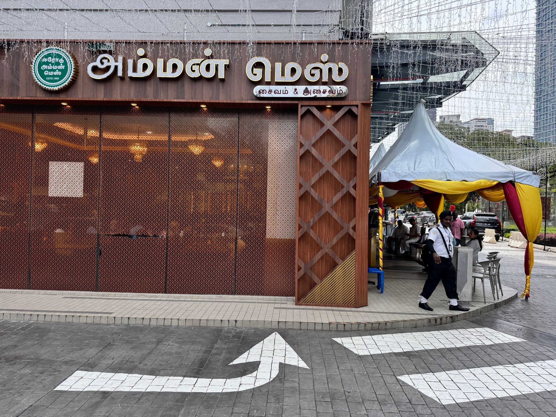 Restaurant exterior with two men seated, motorbike parked.  Pink awning, white building.