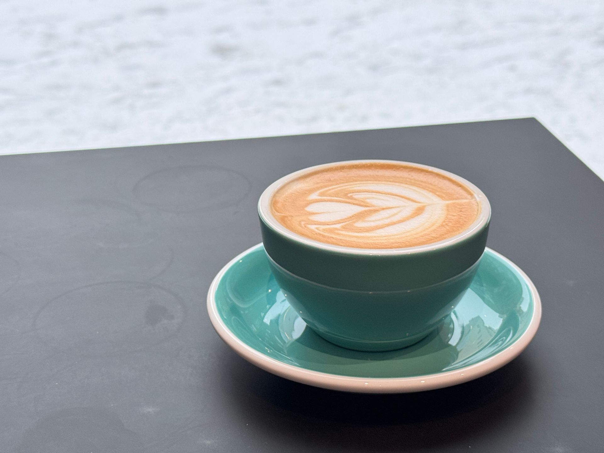 Restaurant exterior with two men seated, motorbike parked.  Pink awning, white building.