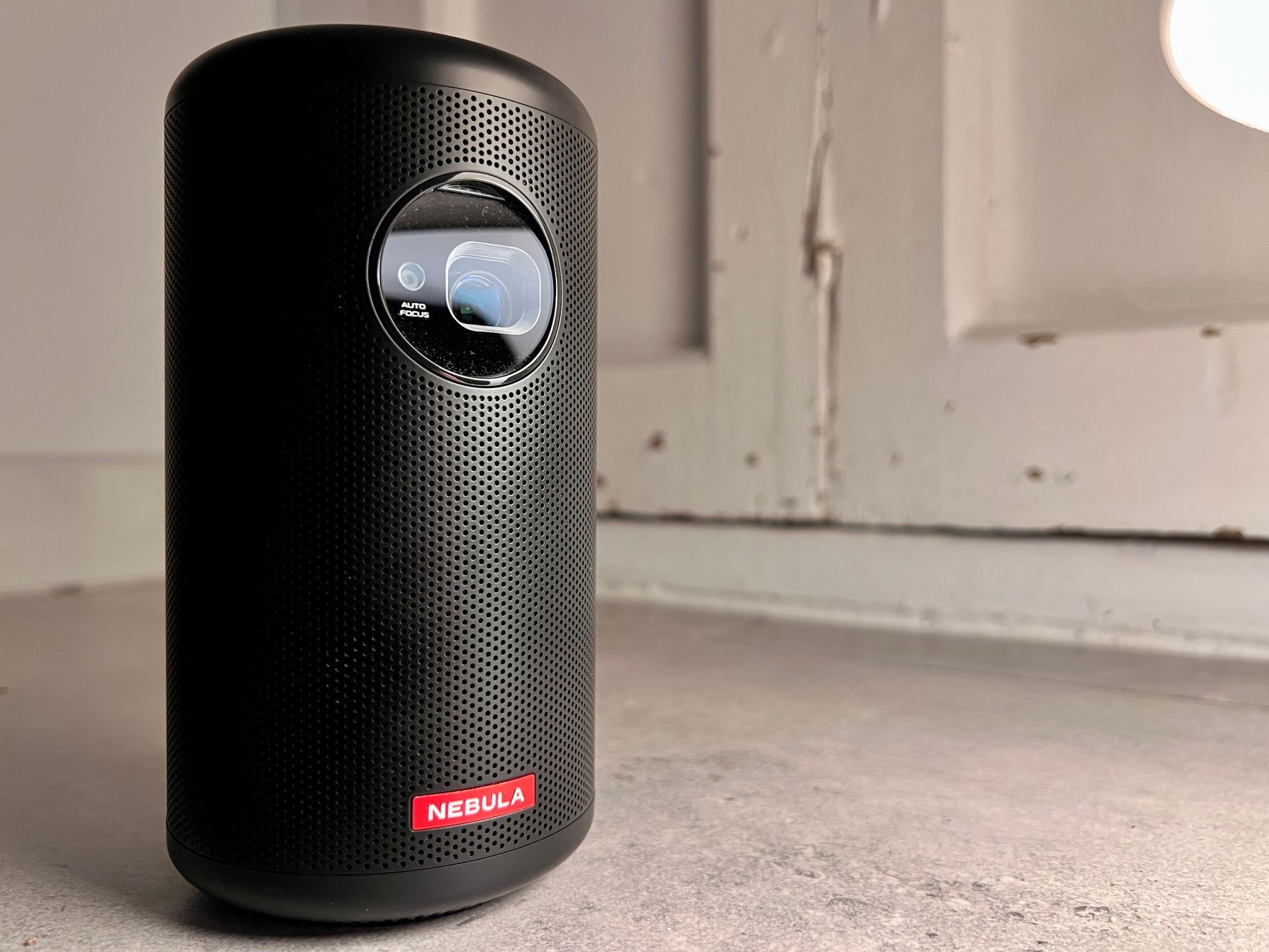 Black cylindrical Nebula projector on a ledge with a red logo.