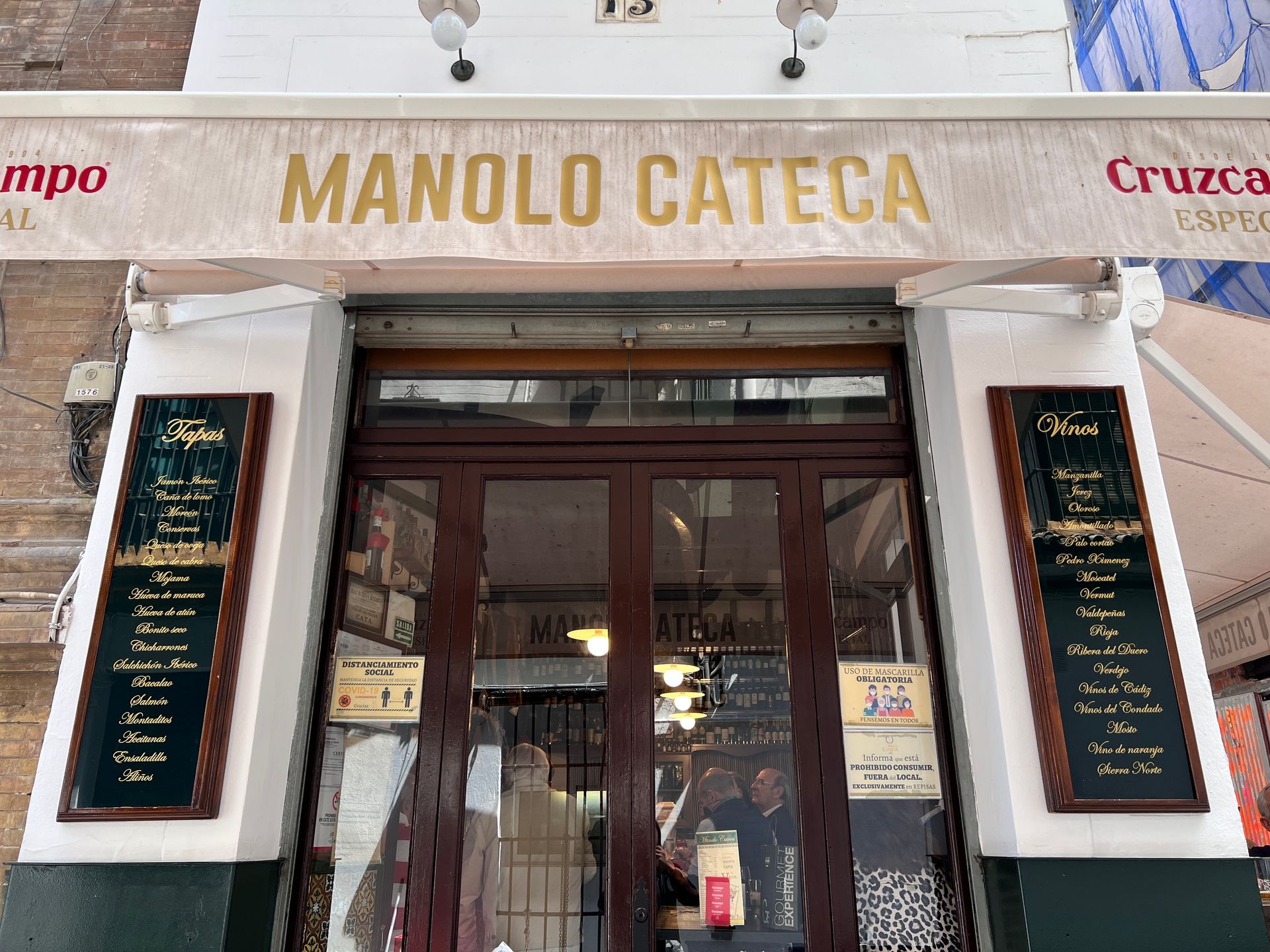 Manolo Cateca restaurant entrance with brown doors, menu boards, and awning in Seville, Spain.