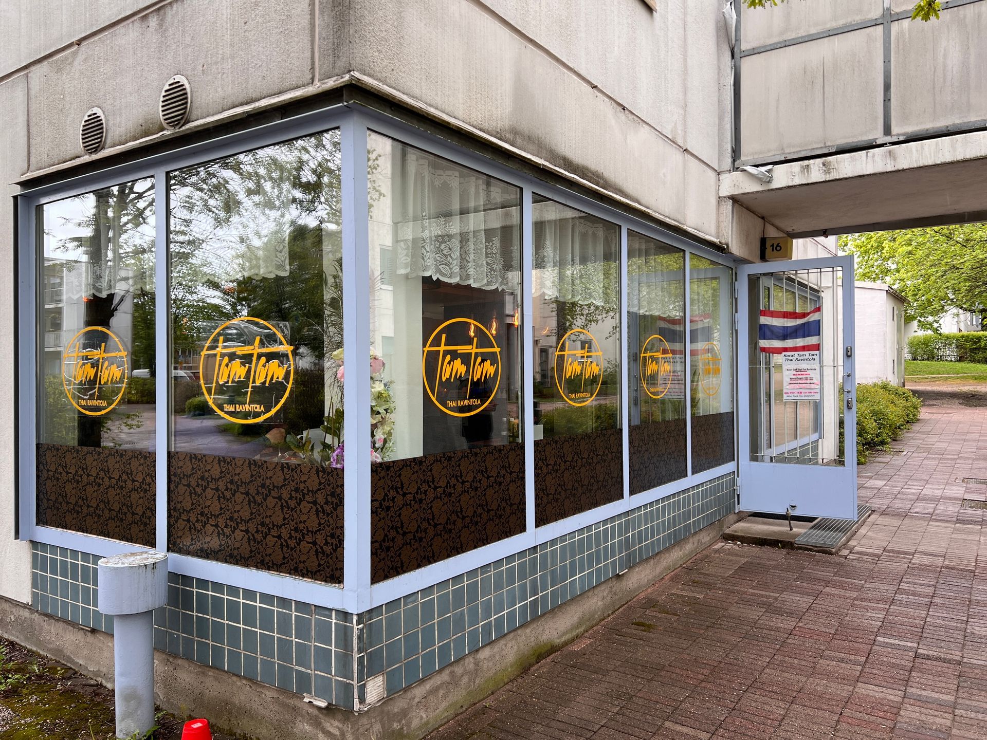 Exterior view of a Thai restaurant with large windows displaying the name in yellow. The door is open.