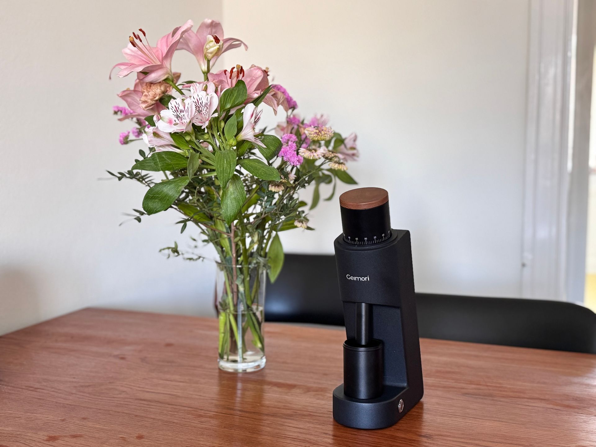 Glass vase of pink flowers beside a black bottle on a wooden table