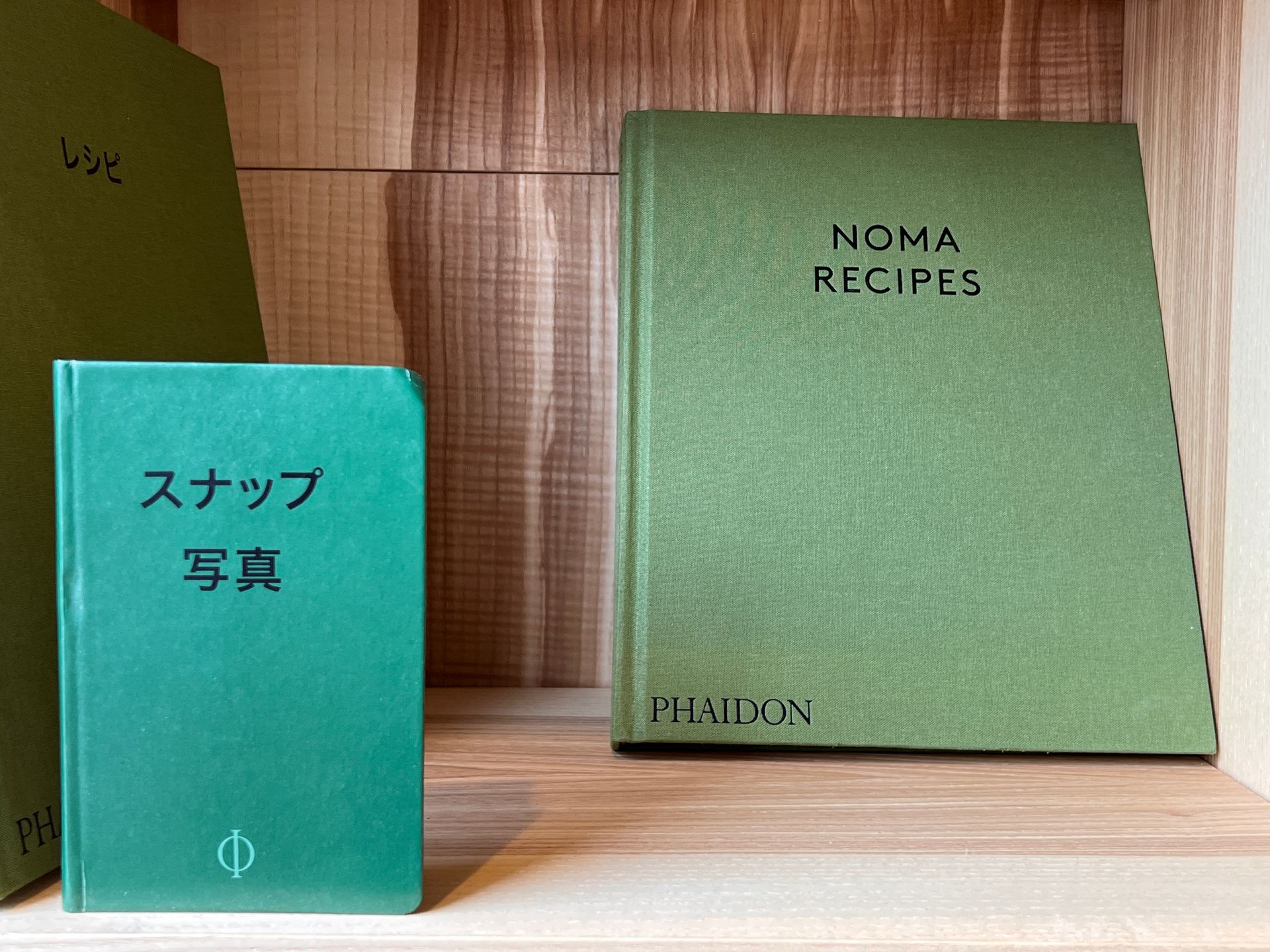 Green books on a wooden shelf. The books have titles in Japanese and English.