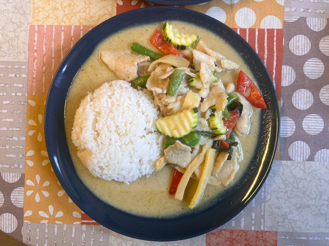 Restaurant exterior with two men seated, motorbike parked. Pink awning, white building.