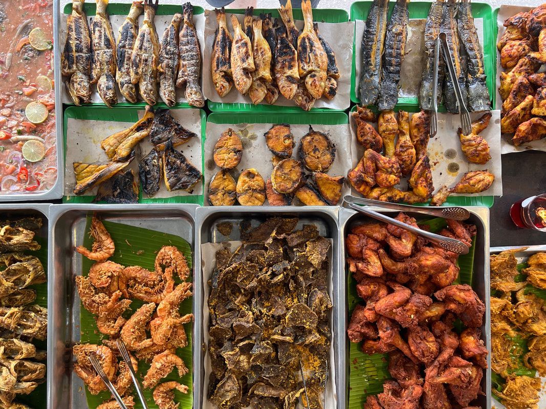 Overhead view of a food display with various fried and grilled seafood, in trays.