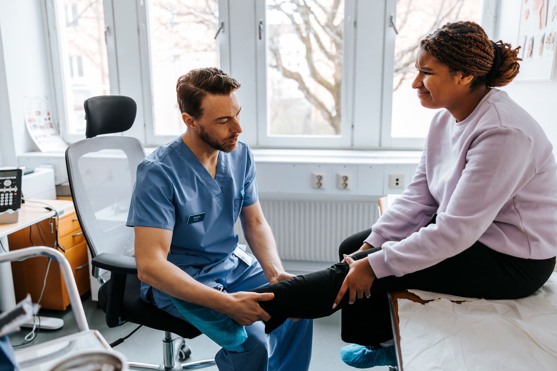 Doctor examines patient's leg during clinical consultation.