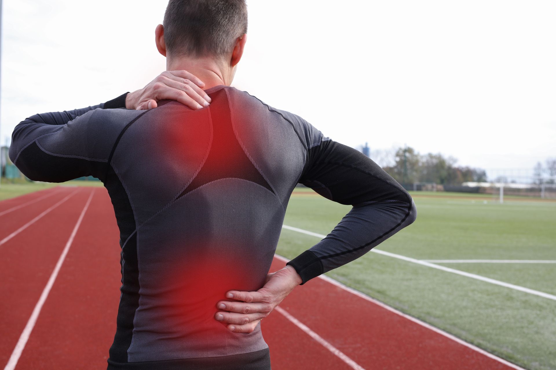 A man is holding his neck and back in pain on a track.