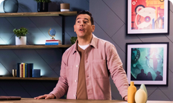 A man in a pink shirt is standing in front of a table.